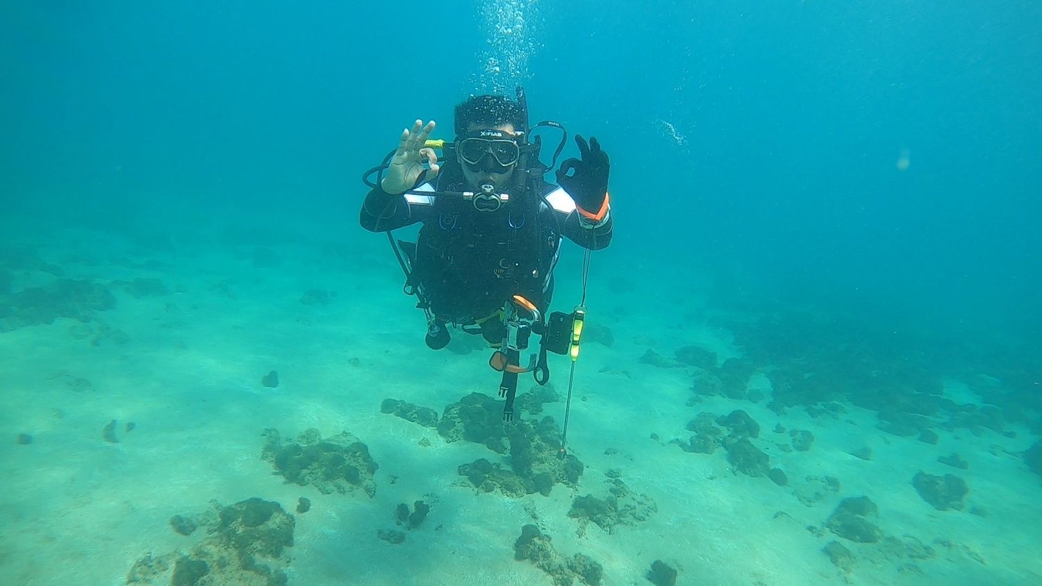 A diver coming towards the camera above a sandy reef in turquoise water