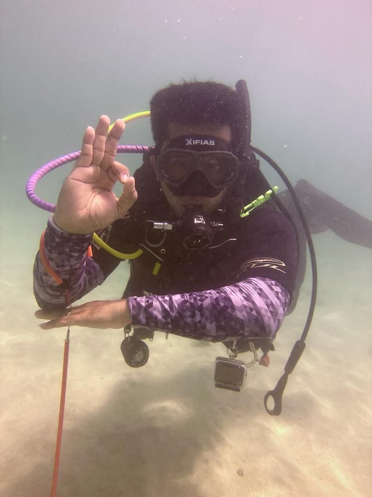 A diver giving an okay sign at the surface, wearing a mask and purple long-sleeve top
