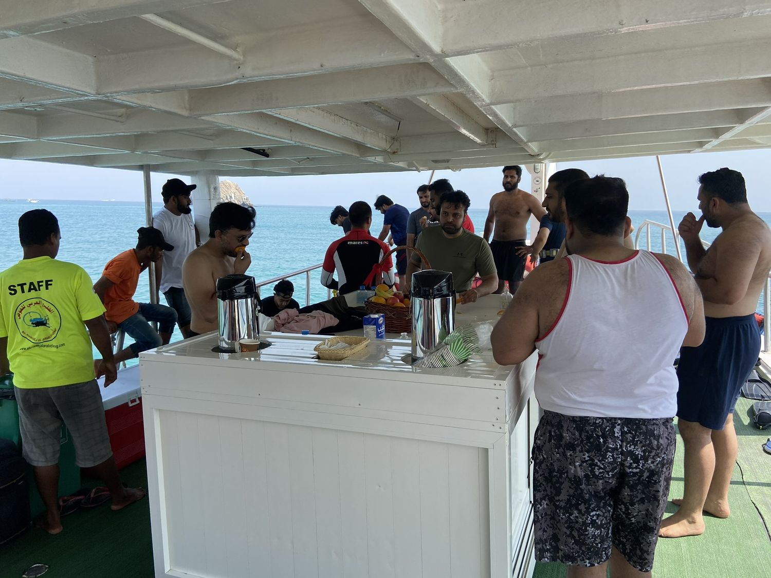A crowded dive boat deck with divers and crew getting ready beside the tank racks