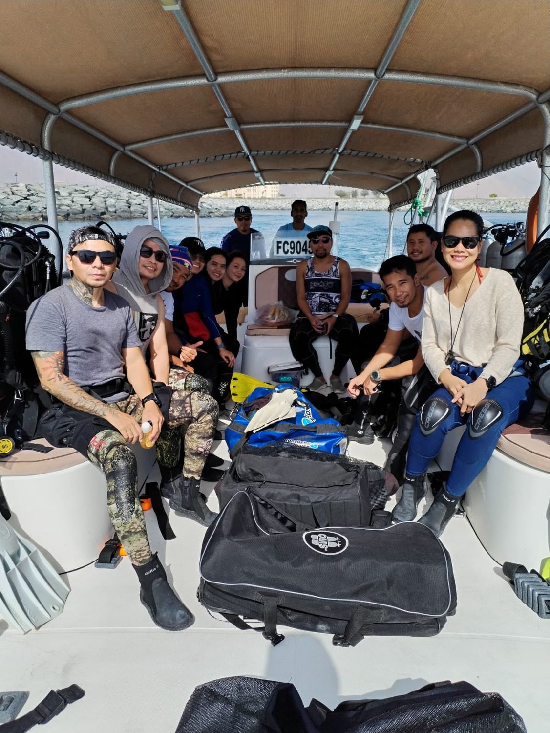 Divers sitting on a shaded boat deck with their gear bags around them, waiting to head out