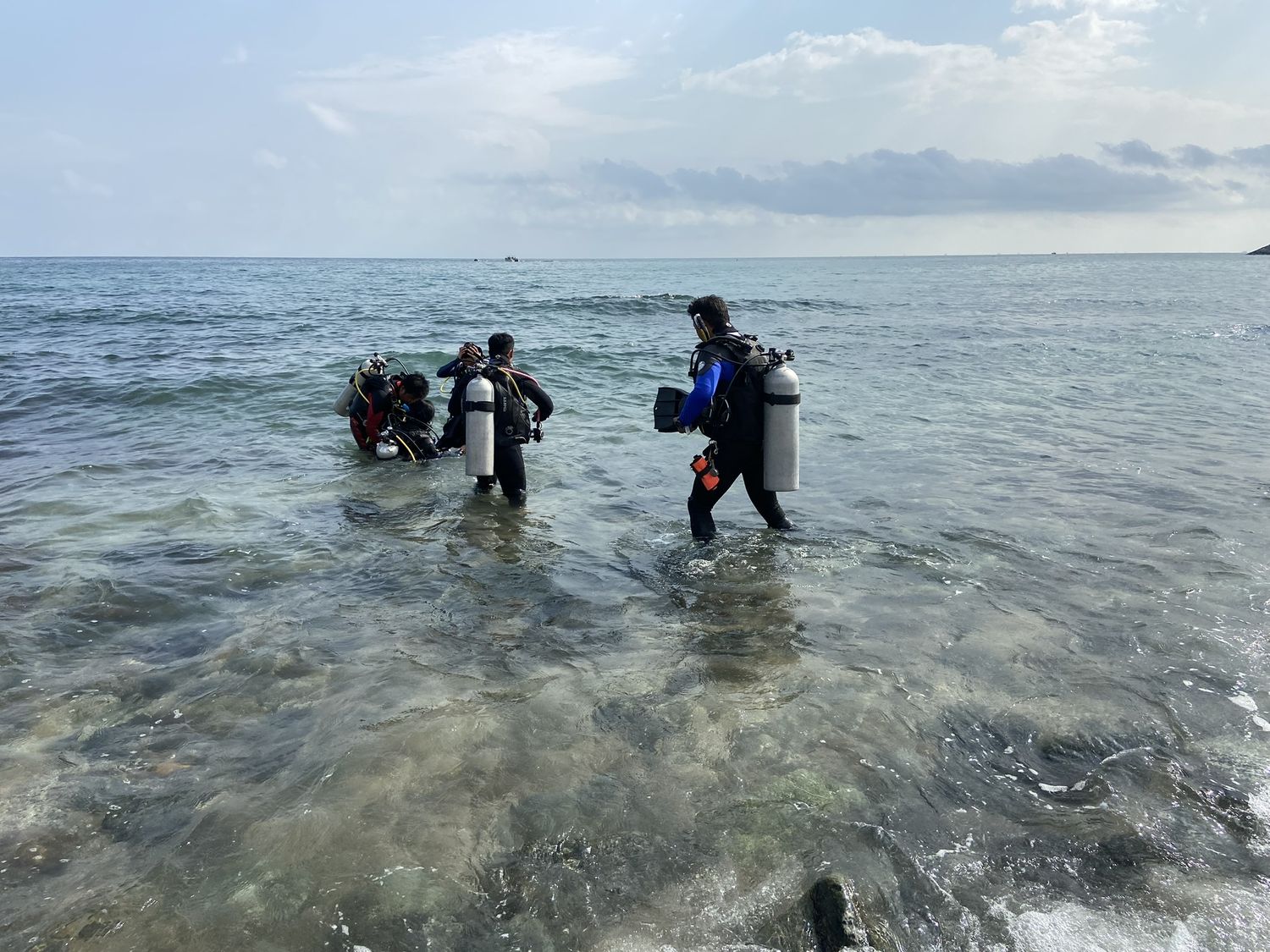 Divers walking out into shallow water with tanks on, a headland in the distance