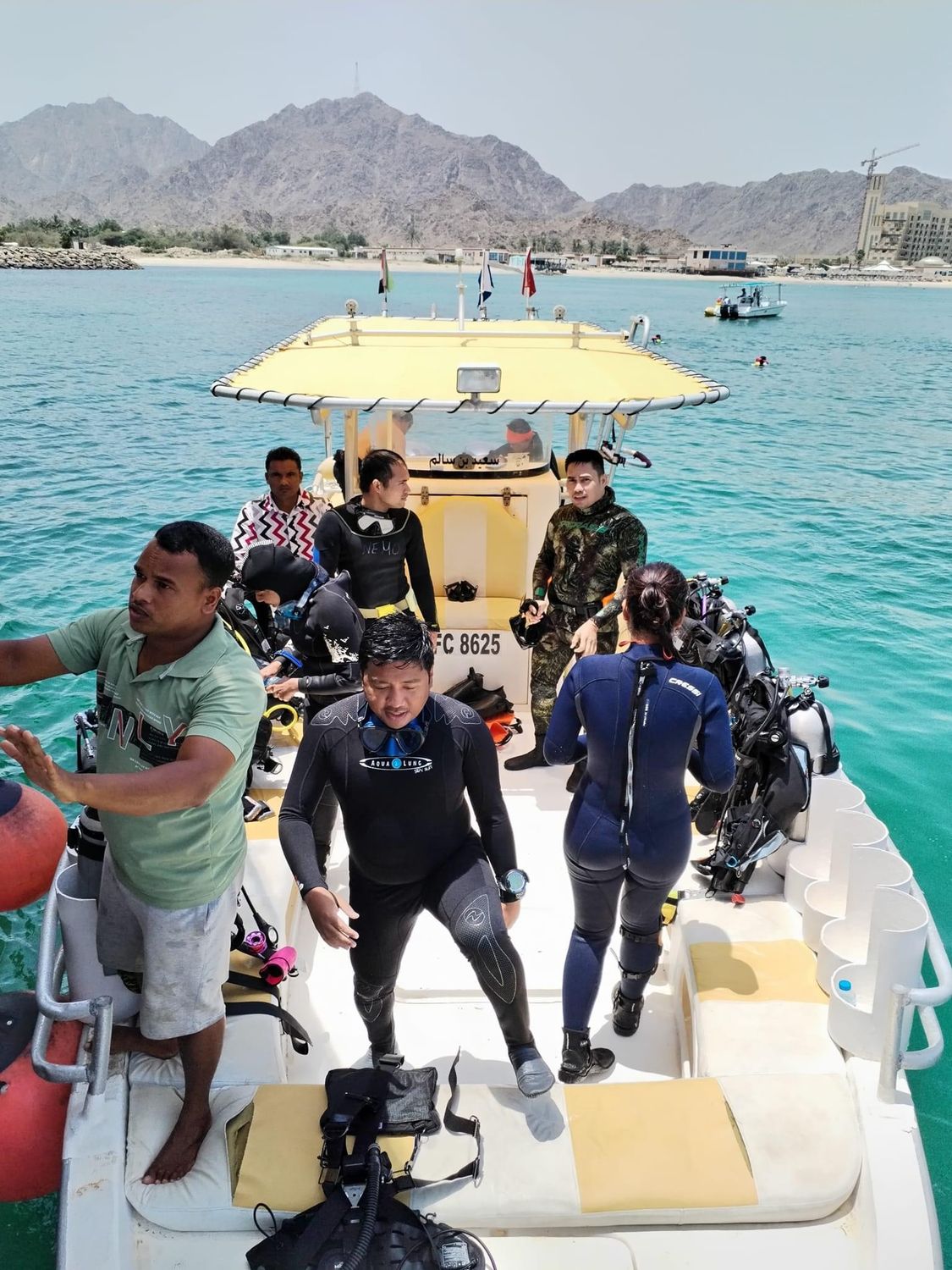 Divers stepping off the back of a yellow dive boat into blue water